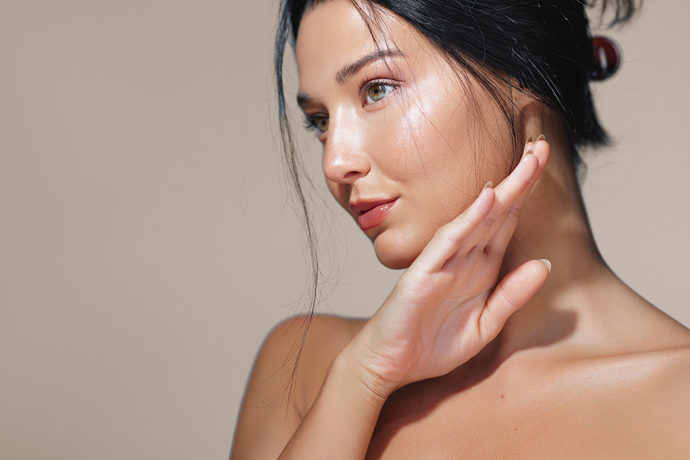 Young woman with glowing skin touching her face